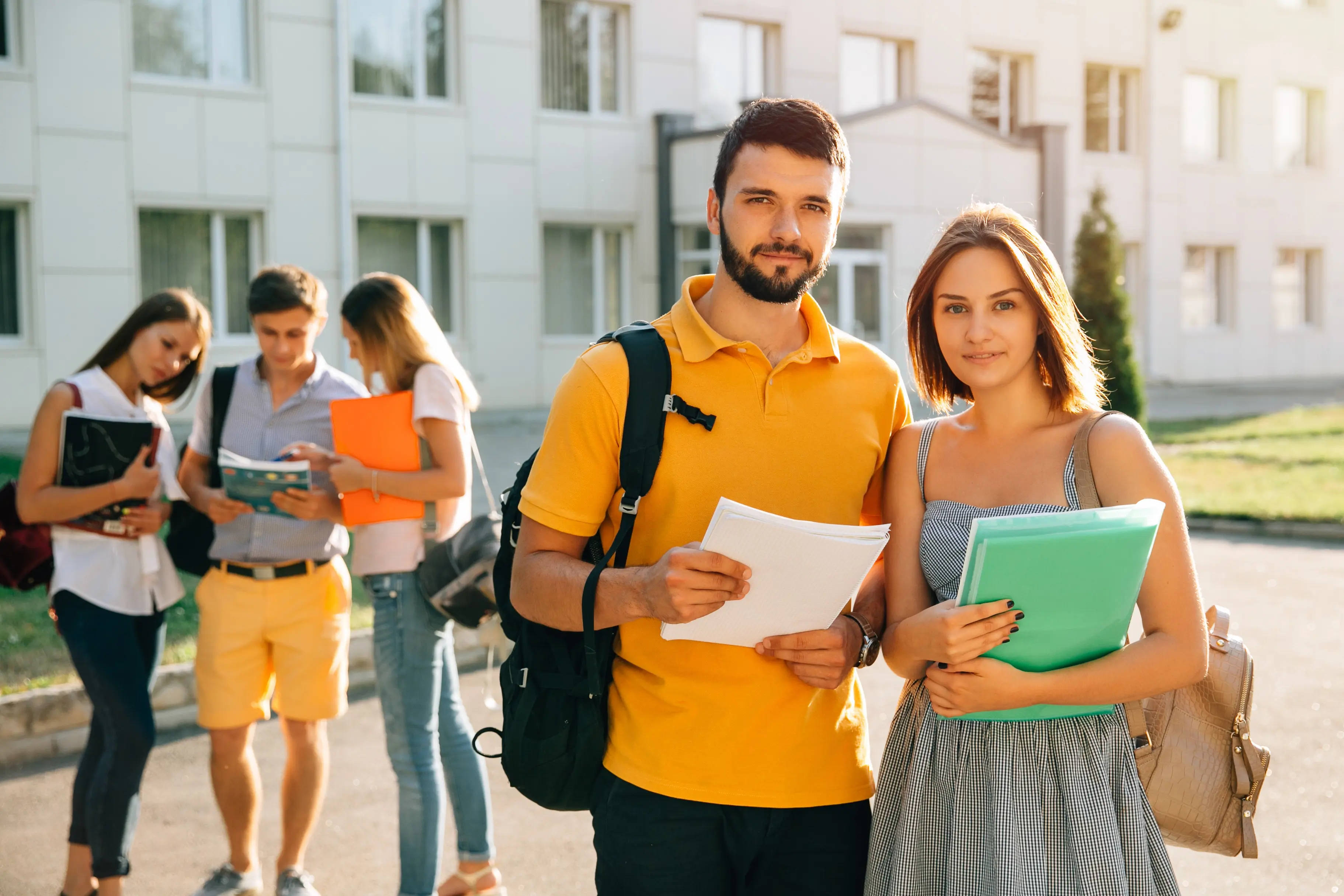 Two happy students with backpacks and books in their hands smiling at the camera